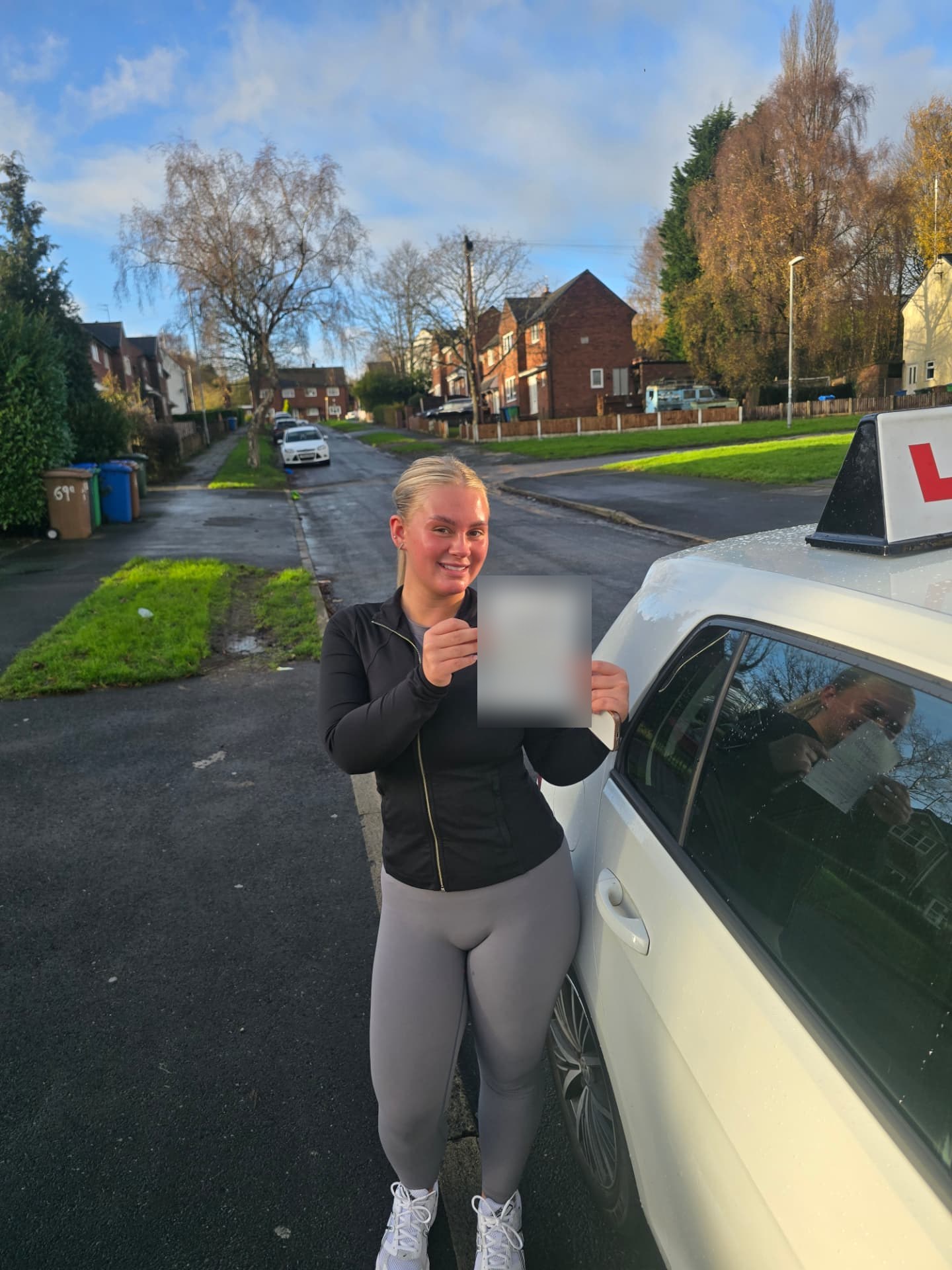 FSK Driving Instructors learner Ameliah holding her practical driving test pass certificate next to the learner car in Chadderton