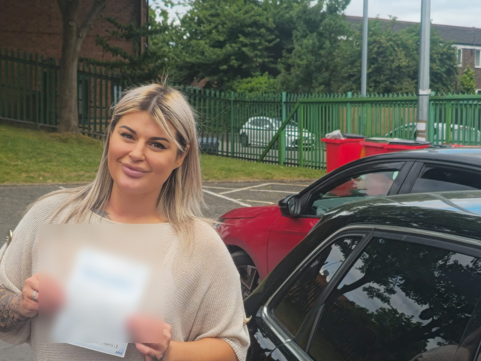 FSK Driving Instructors learner Rebecca Hughes holding her practical driving test pass certificate next to the learner car at Cheetham Hill test centre