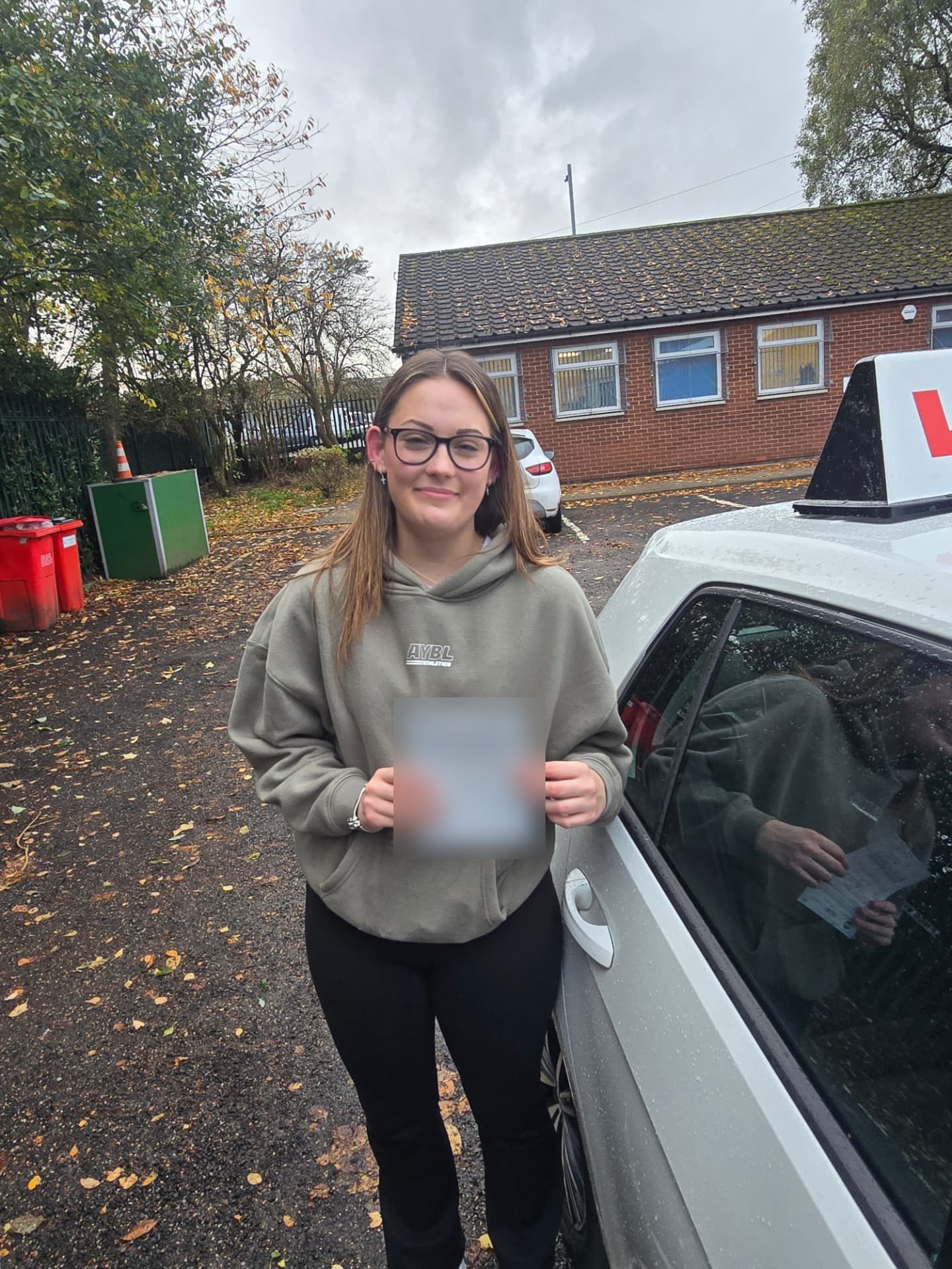 FSK Driving Instructors learner Madeleine holding her practical driving test pass certificate next to the learner car in Bury