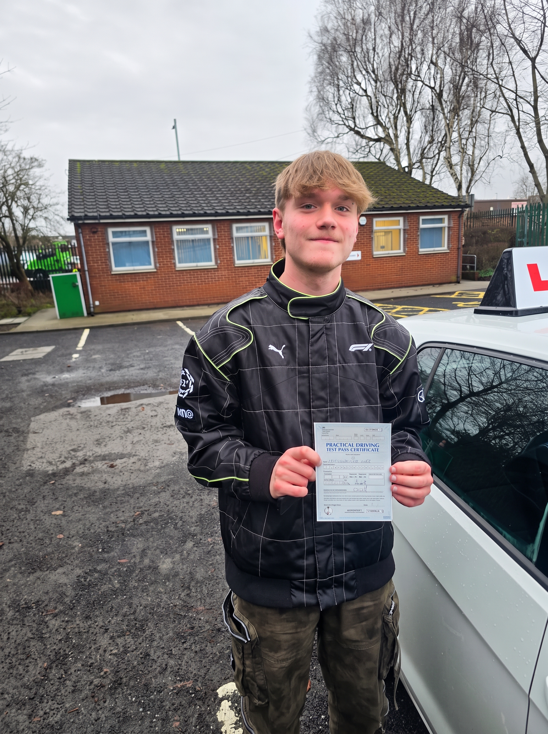 FSK Driving Instructors learner Alexander holding his practical driving test pass certificate next to the learner car in Bury