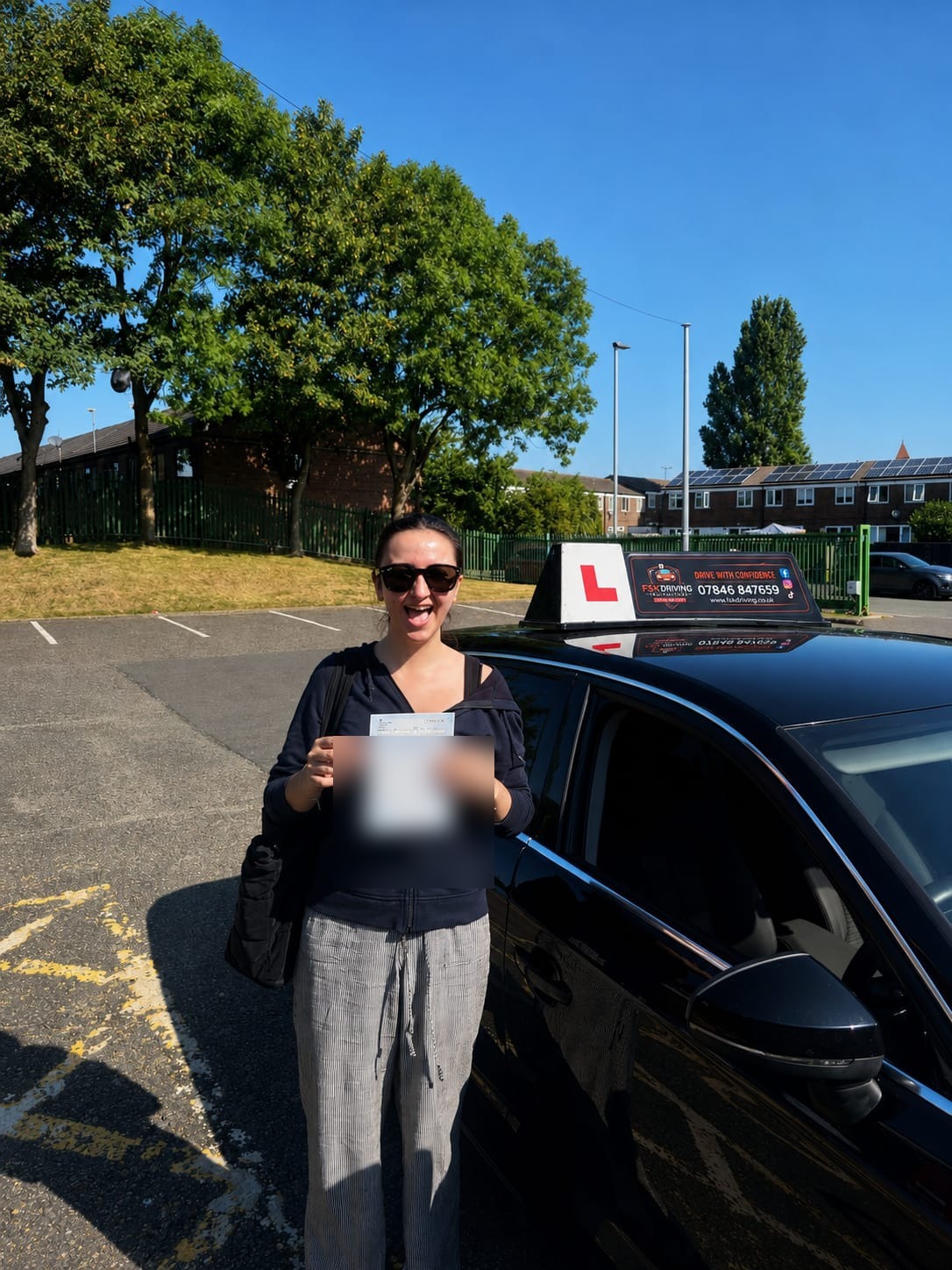 FSK Driving Instructors learner Samiya holding her practical driving test pass certificate next to the learner car at Cheetham Hill test centre