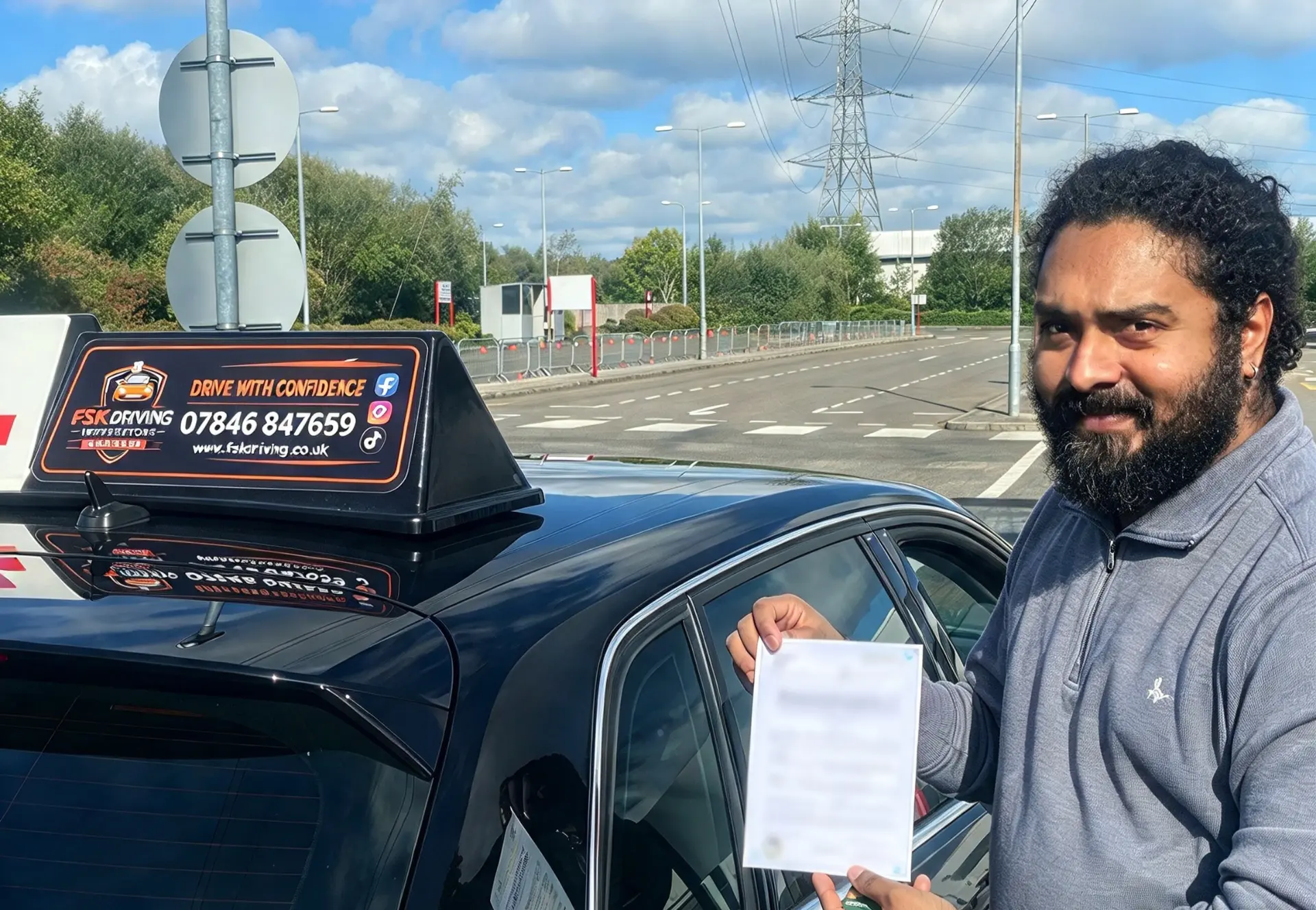 FSK Driving Instructors learner Anu holding his practical driving test pass certificate next to the FSK learner car after passing at Chadderton test centre