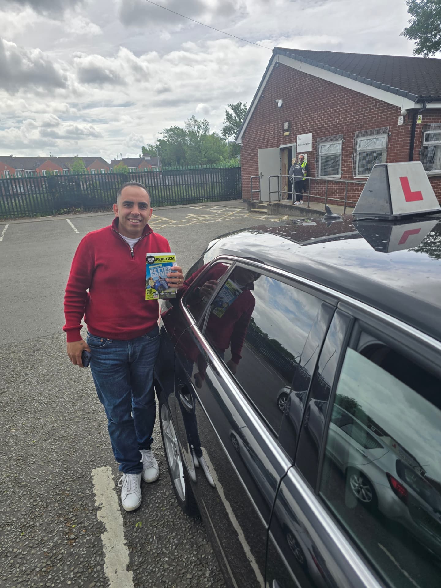 FSK Driving Instructors learner Poula holding his practical driving test pass certificate next to the learner car at Cheetham Hill test centre